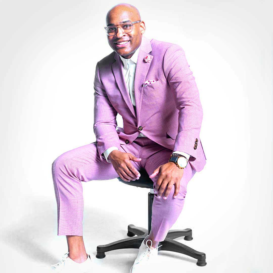 A man in a pink suit, working as a DJ in Atlanta, sitting on a chair.